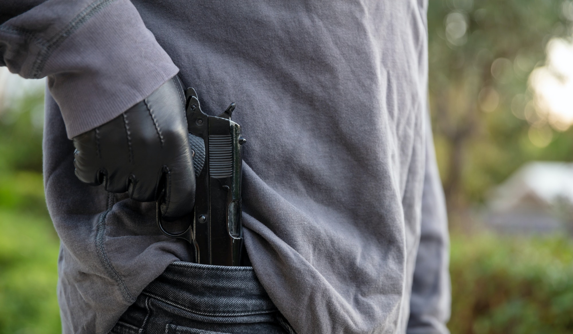 gloved-hand-holding-a-pistol-blur-nature-background-.jpg